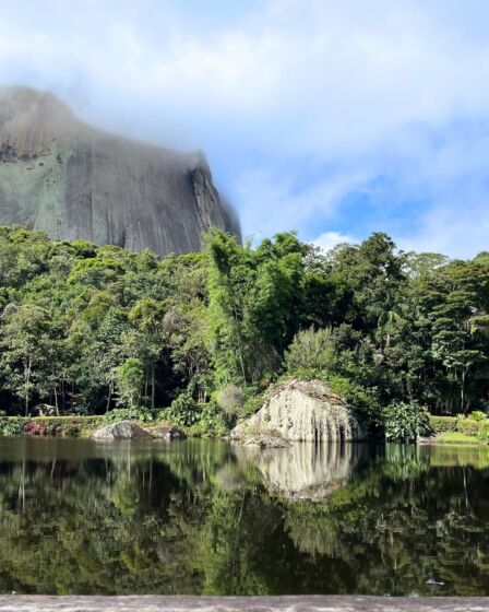 Lindo lago com vegetação na parte do meio da imagem e uma pedra enorme no fundo da imagem
