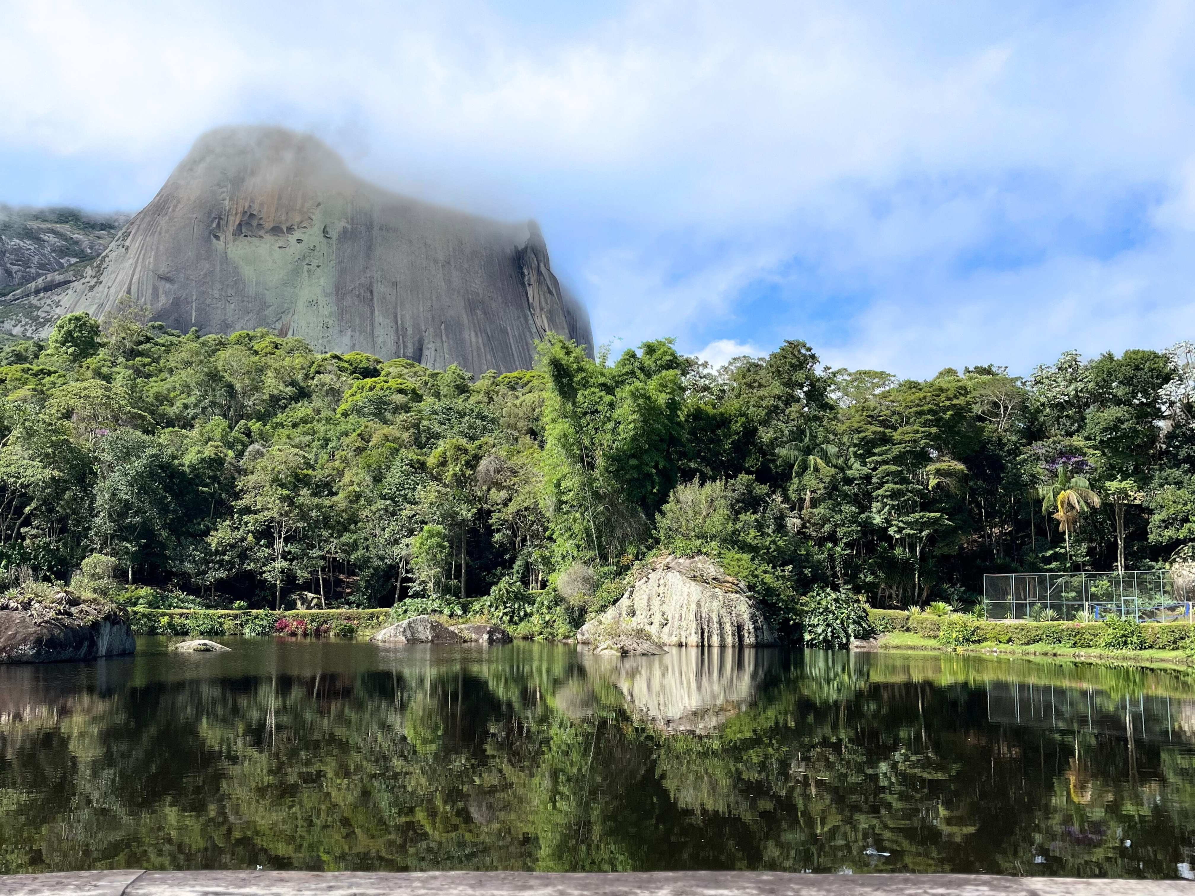 Lindo lago com vegetação na parte do meio da imagem e uma pedra enorme no fundo da imagem