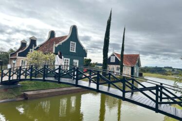 mulher atravessando uma ponte sobre um rio com casas no formato holandês ao fundo