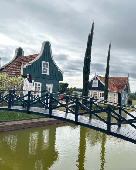 mulher atravessando uma ponte sobre um rio com casas no formato holandês ao fundo