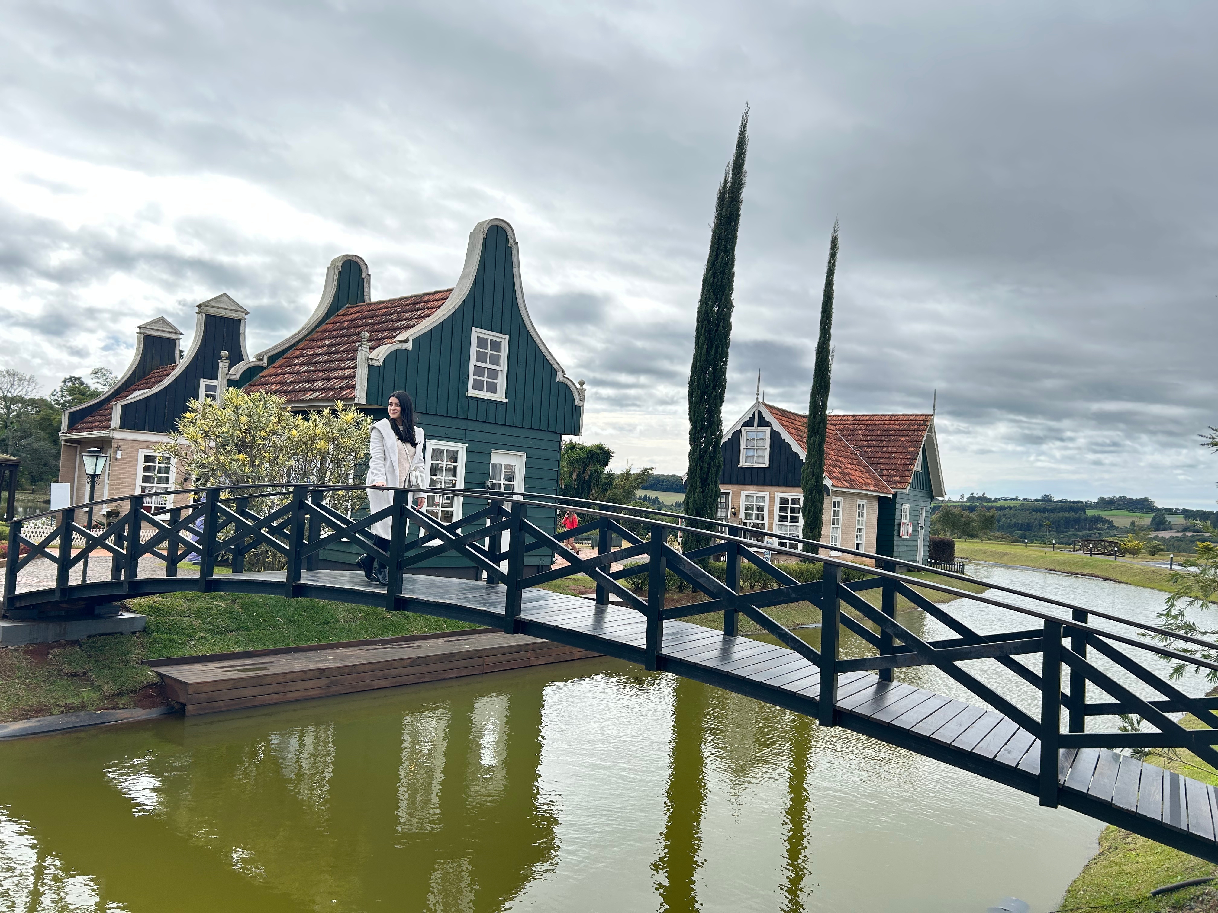 mulher atravessando uma ponte sobre um rio com casas no formato holandês ao fundo